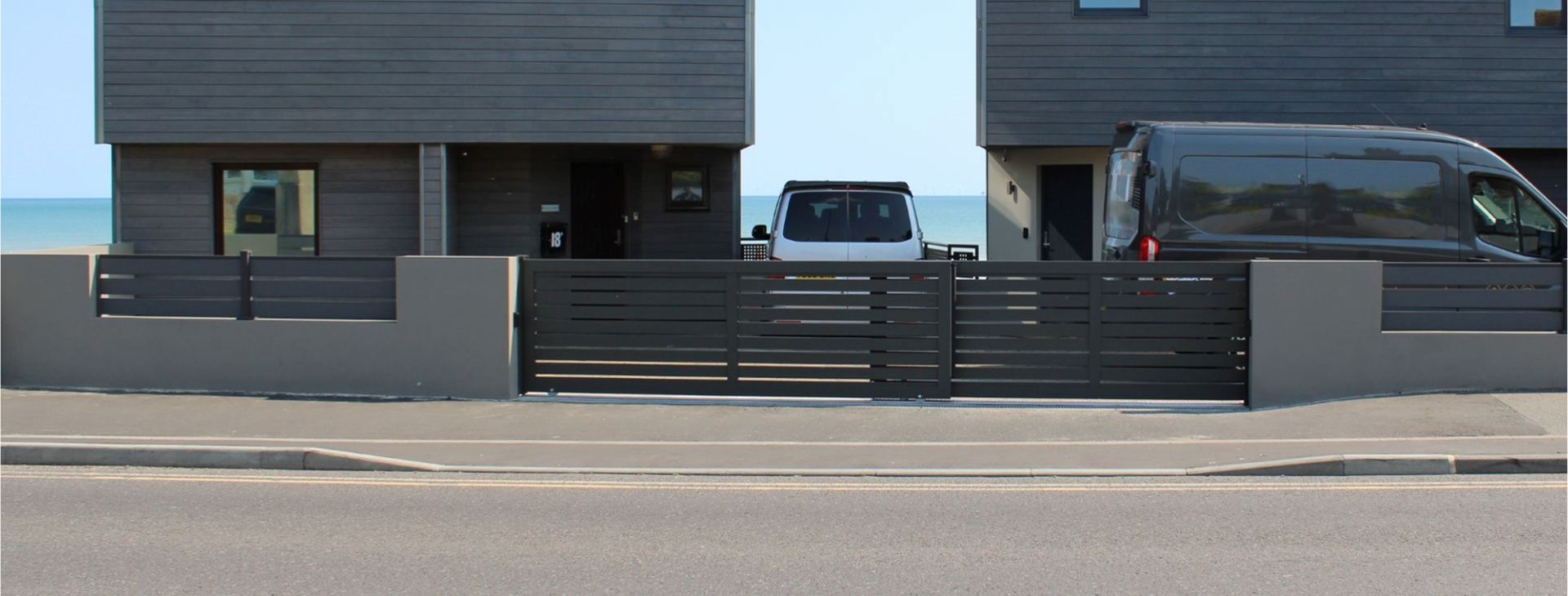A dark grey aluminium gate from TFS Gates, which is installed on a driveway by the seaside